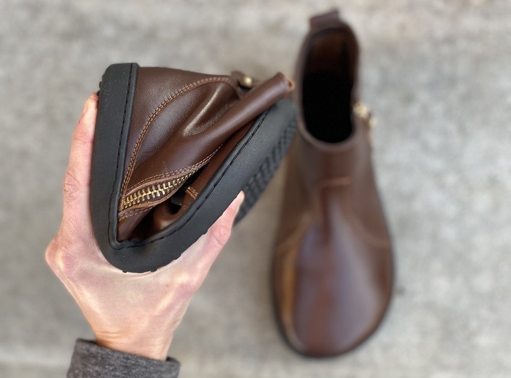 Close up of a hand holding a Shapen Ivy barefoot dress boot showing the flexibility of the zero drop outsole.