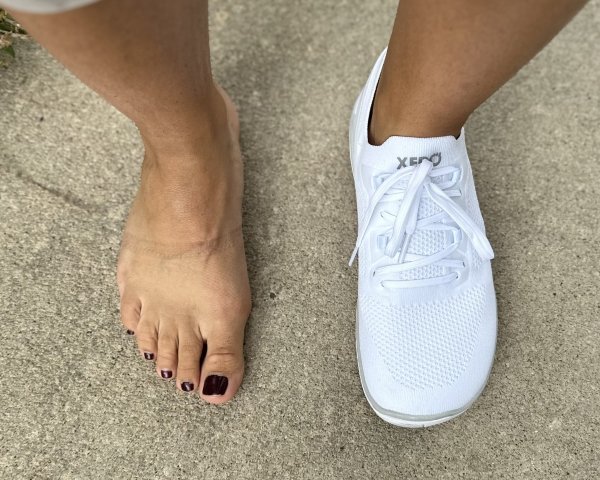 Top down view of a person with 1 bare foot and the other wearing Xero Shoes Nexus casual barefoot sneakers in white knit with a wide comfortable toe box