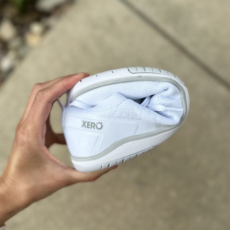 Close up of a hand holding a Xero Shoes Nexus barefoot sneaker into a U shape to show the flexibility of the zero drop outsole and stretchy uppers