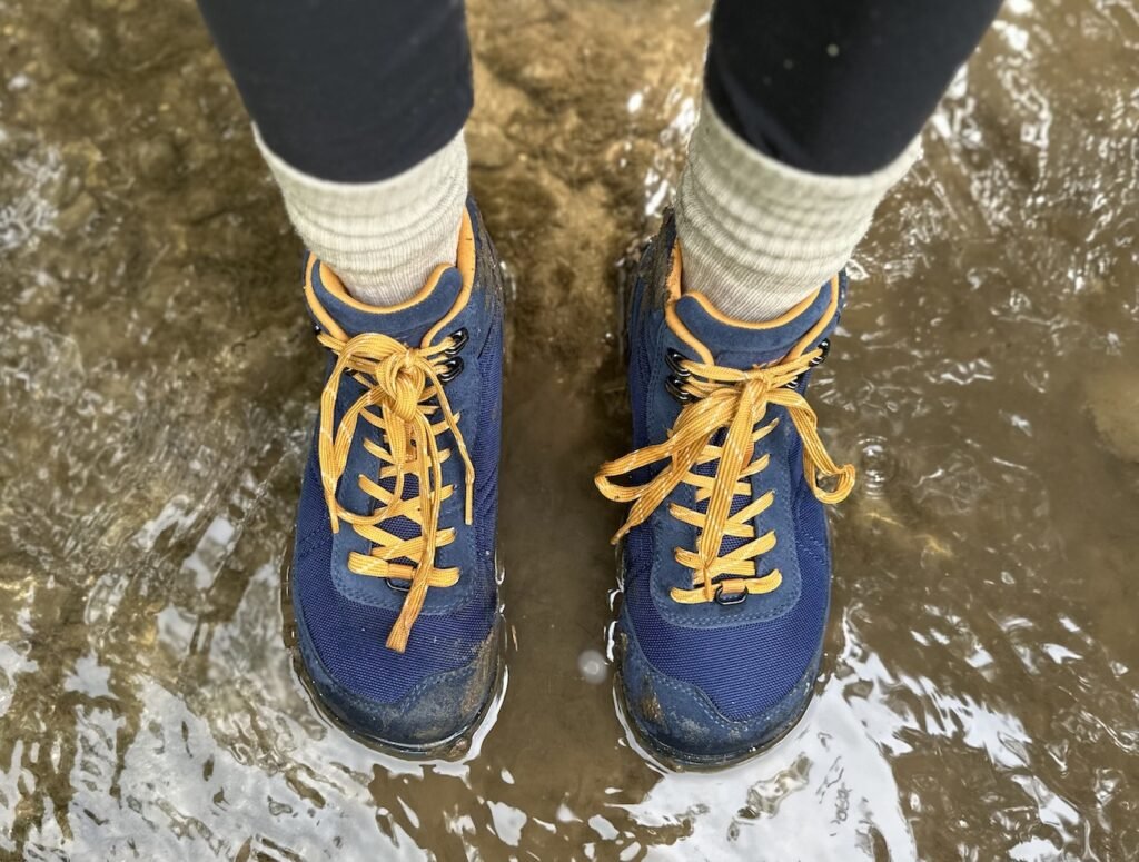 Top down view of Xero Shoes Ridgeway hiking Shoes being worn in water. You can see the speed hooks, golden laces against navy uppers, and the wide anatomical toe box