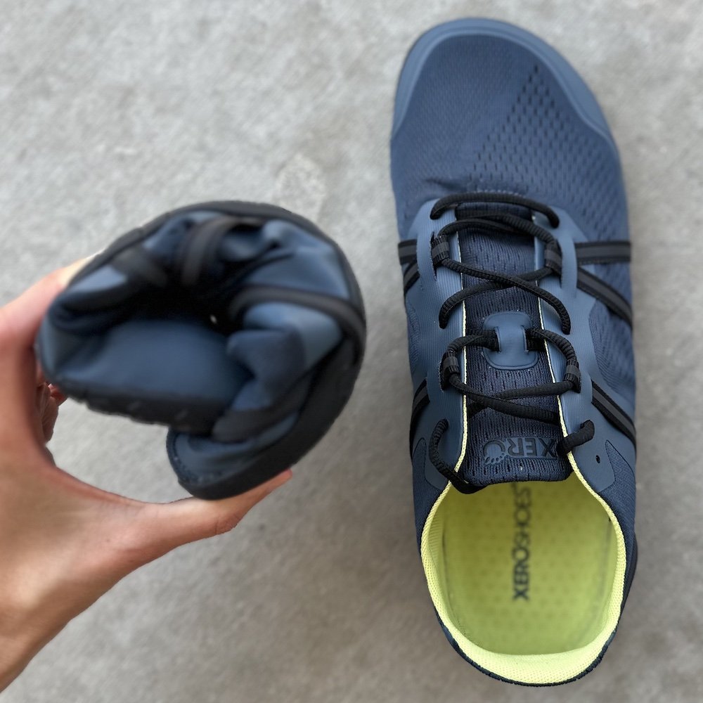 a close up of a hand holding a rolled up Xero speedforce 2 mens barefoot running shoe to show its flexibility