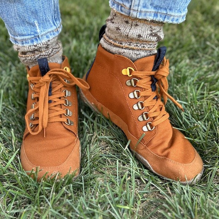 Front close up of a pair of feet in Wildling Tejo caramel waterproof barefoot boots. The foot on the right is lifted slightly and turned to the side to show the profile with speed lace eyelets for easy on/off