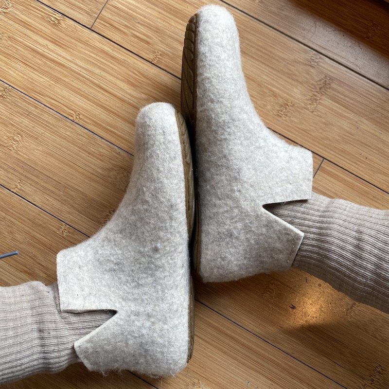 a top down view of a pair of feet with soles touching wearing wool socks and wool Wildling shoes barefoot slippers Lotus in a cream color and a rubber outsole