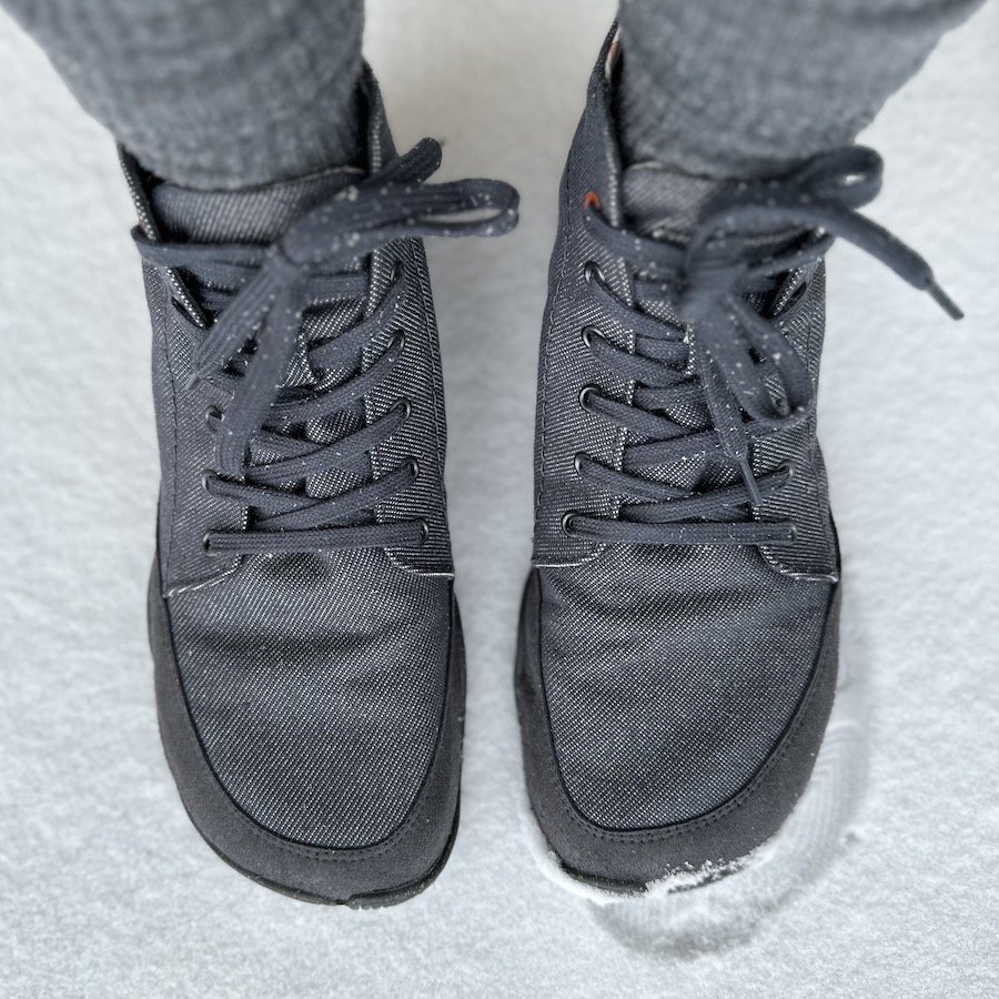 A top down view of a pair of feet standing in snow wearing Wildling shoes Arni grey vegan barefoot shoes for fall winter