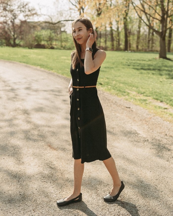 Full body photo of a woman in a black dress walking to the left wearing Be Lenka Bellissima flats outside in the sunshine on a gravel road