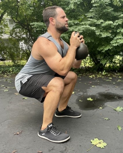 A muscular man doing a solid weighted squat wearing Freet Vibe, zero drop sneakers for balance and foot function