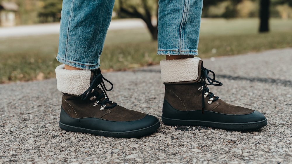 Close up of a person walking in Shapen Barefoot Lynx barefoot boots with a turned down fuzzy cuff, eyelets, and a reinforced toe box edge. The no heel zero drop outsole is flexible and thin for optimal foot function.