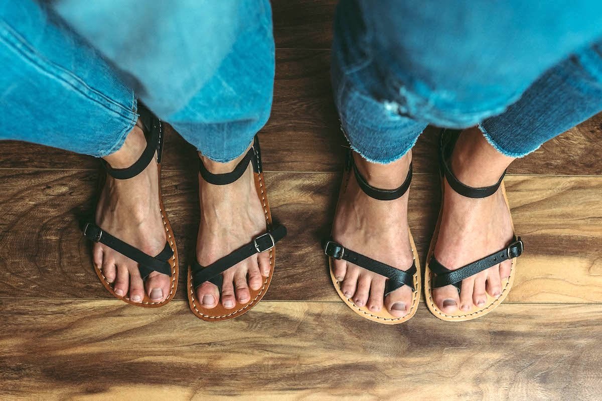 two pairs of feet standing side by side both wearing black Crupon sandals Nomade, with one in barefoot width and the other in Extra wide width