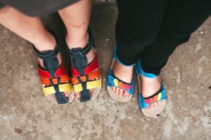 Two kids standing side by side with their feet visible wearing kids colorful barefoot summer sandals from Zeazoo