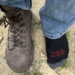 Top down close up view of a man with 1 Carets Determination Safety steel toe boot on, and one socked foot to show the wide toe box that won't squish toes
