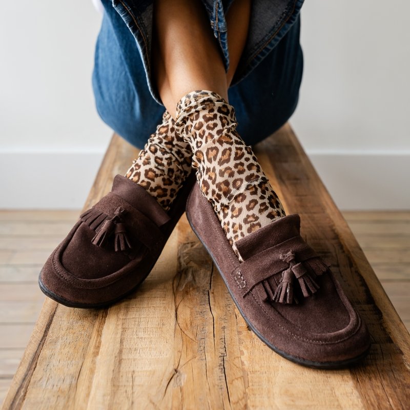 Front view of a peron with crossed feet wearing sheer leopard socks and be Lenka Fiorela brown suede loafers with a wide comfortable toe box