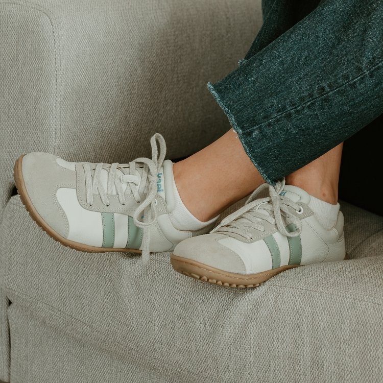 A person's crossed legs wearing dark denim and Koel Ila in leather with green and beige accents