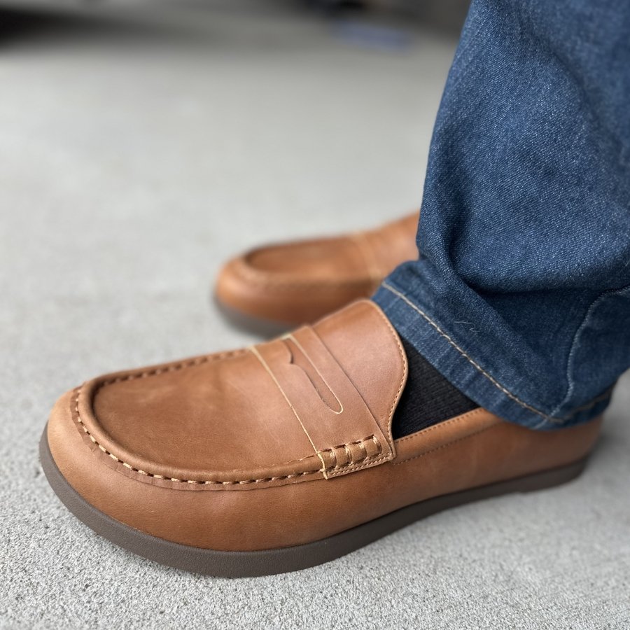 Side view of a man's feet in Oaka loafers in light brown leather with stitching details, and a flat flexible outsole