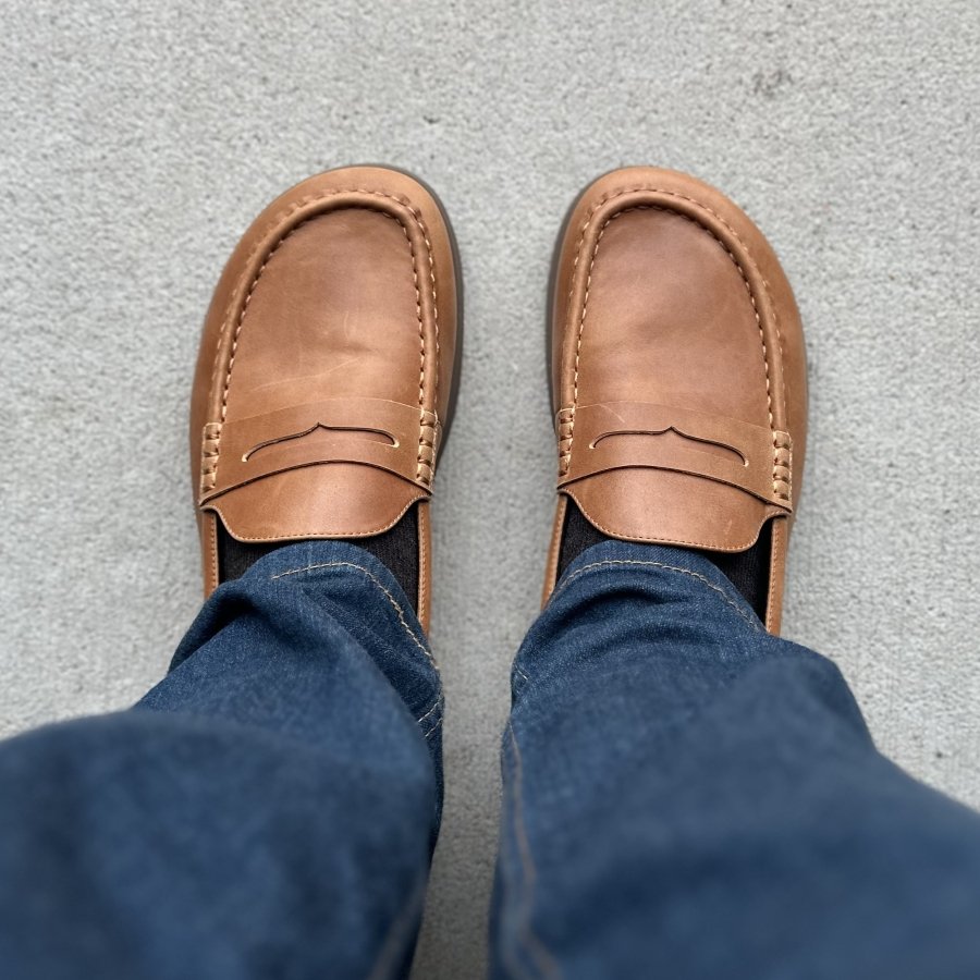 Top down view of a man's feet in Oaka barefoot loafers in a light brown leather with stitching and penny loafer details