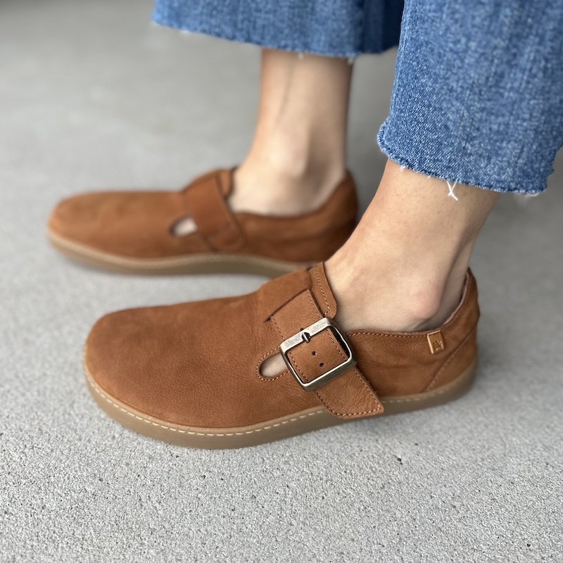 Side close up view of a pair of light brown leather El Naturalista clogs with a single buckle and flat outsole