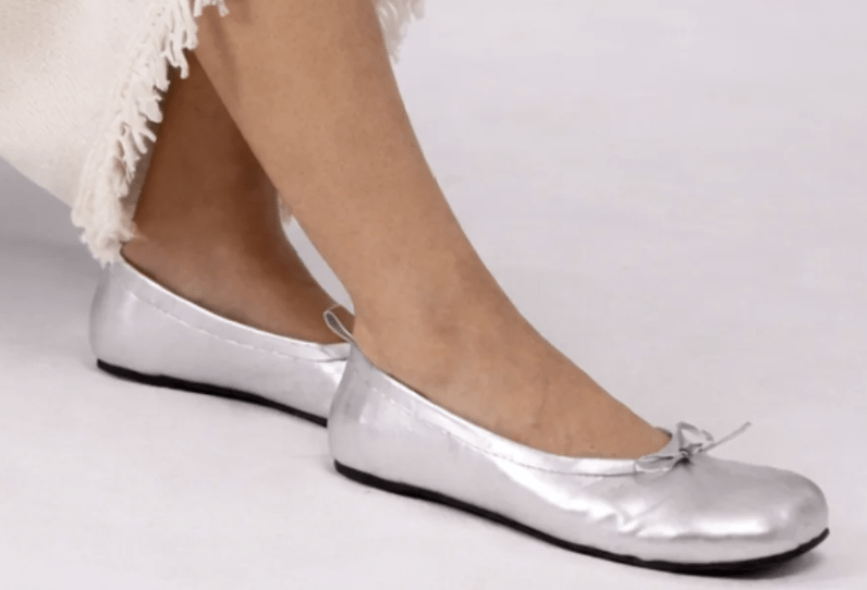 Navega barefoot silver dressy flats being shown with the edge of a white fringed dress.