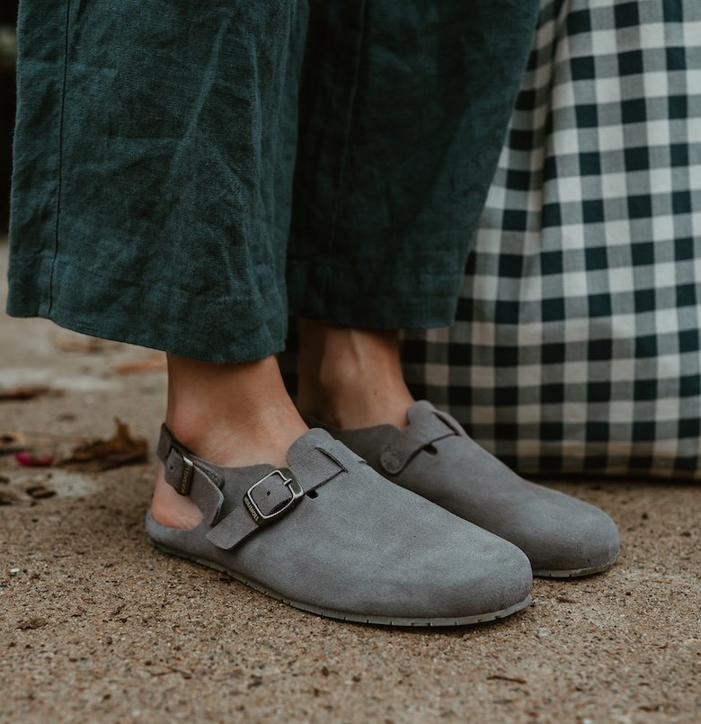 Close up view of grey Mukishoes Soca barefoot clogs worn with dark green linen pants
