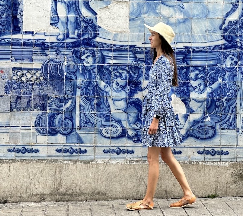 A woman walking in front of blue portuguese tiles azulejos wearing Origo shoes by Anya huarache sandals