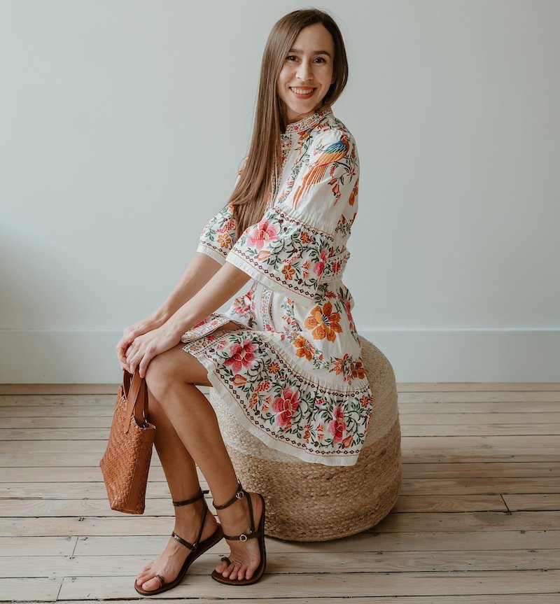A woman sitting down inside wearing a colorful dress and High Feels barefoot sandals that are sexy and dressy but flat
