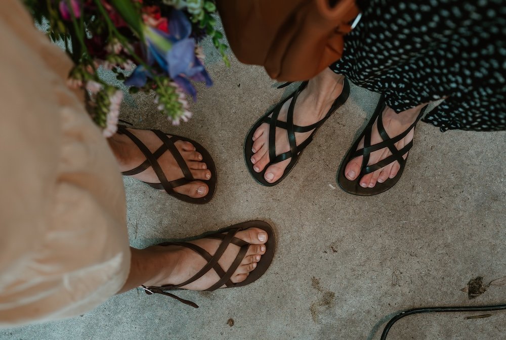 A top down view of two pairs of feet standing toe to toe wearing Laboo Leather barefoot sandals in black and brown leather