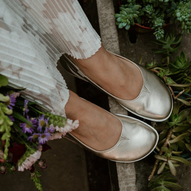 Close up of the toe wide anatomical toe box on Be Lenka Belissima leather barefoot ballet flats being worn by someone resting their feet on the edge of a wall. Pretty potted plants are visible on the right, and a fancy pleated on the left