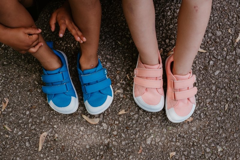 Two pairs of feet resting on the ground wearing Be Lenka Canvi sneakers in blue and pink. The wide toe box has a protective rubber bumper and both pairs have velcro closures.