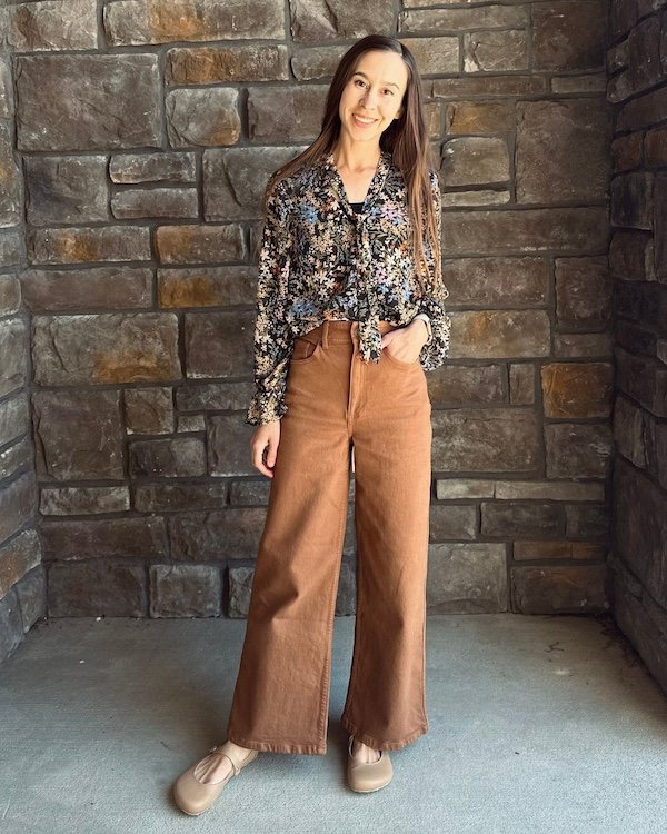 A woman smiling at the camera wearing a stylish outfit with wide leg jeans and beige Jenon Leather Villet barefoot mary janes with a wide toe box
