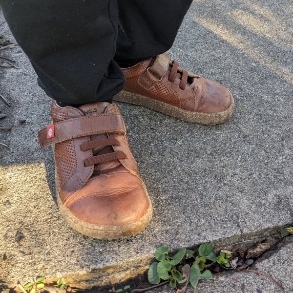 A young child wearing brown leather sneakers from Lang S by Tikki Shoes outside on a sidewalk.