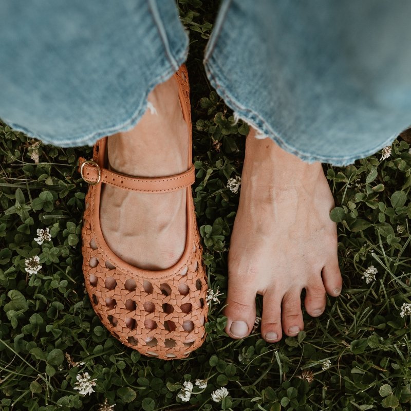 Top down view of a pair of feet with one foot wearing Origo Woven Ballerinas in cognac leather. One foot is bare to show the shape match with the anatomical barefoot shoe