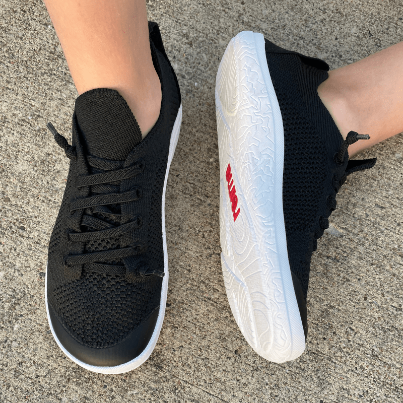 A pair of feet in Reima barefoot knit sneakers with a wide toe box. The foot on the right is resting on its side to show the zero drop outsole