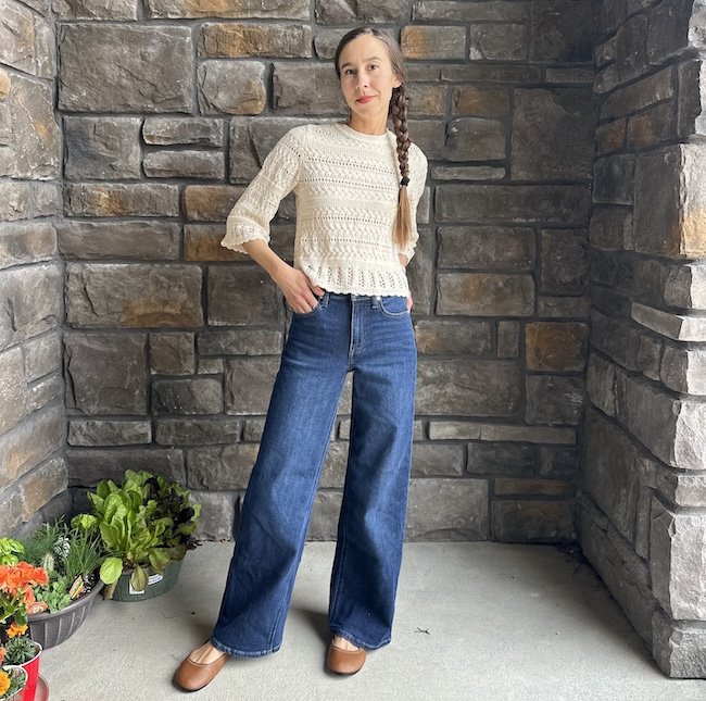 A woman posing for the camera wearing a knit top, wide leg pants, and brown leather barefoot ballet flats - the Softstar Ballerine ankle strap