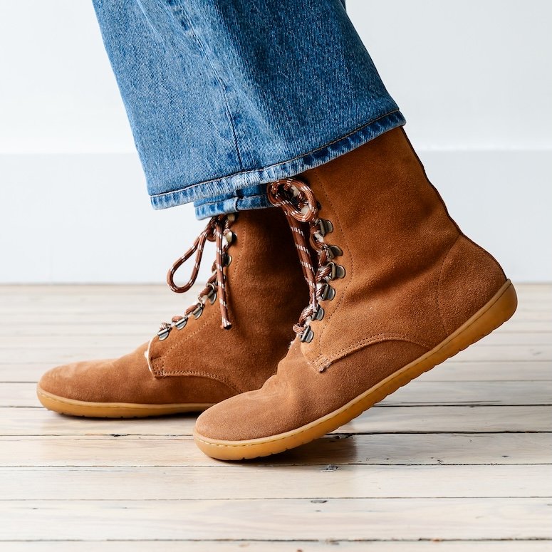 Side view of a person's legs in medium wash denim with a pair of Mukishoes Lapedo furry brown suede barefoot boots with a wide toe box and striped laces.