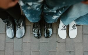 Top down view of a line of 3 women in Peerko lace up boots. Three colors including a metallic cosmic, patent black leather, and matte white boots are lined up with wide toe boxes the focus off the frame.