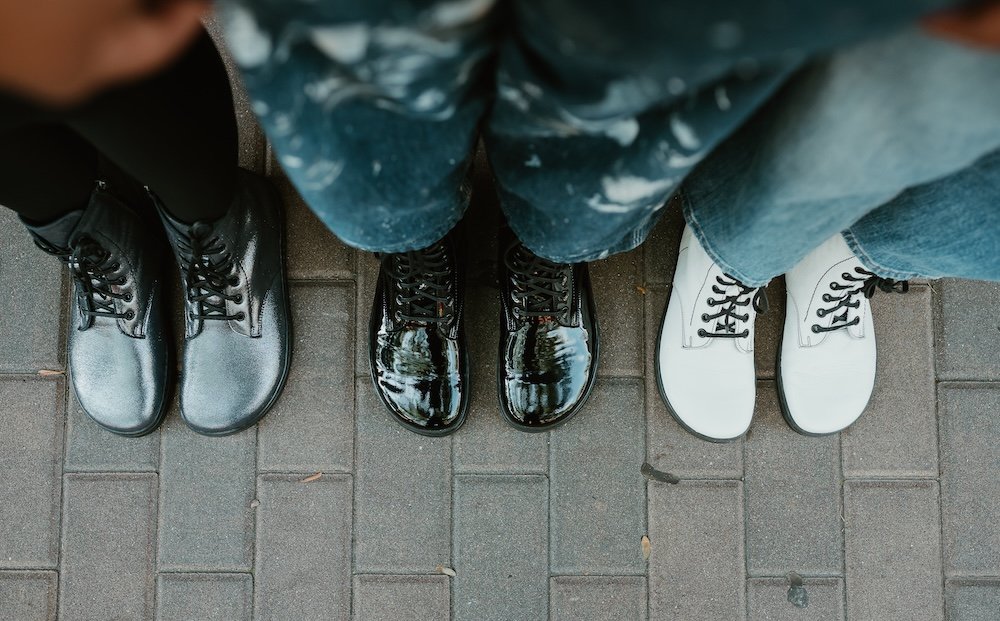 Top down view of a line of 3 women in Peerko lace up boots. Three colors including a metallic cosmic, patent black leather, and matte white boots are lined up with wide toe boxes the focus off the frame.