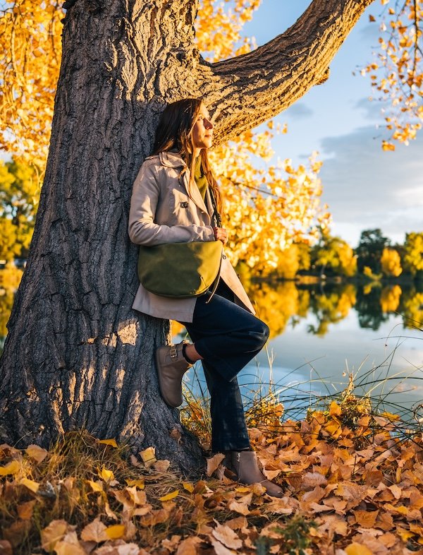 A woman leaning against a tree with golden leaves all around wearing Xero Shoes Tari II Doeskin barefoot chelsea boots designed with Anya