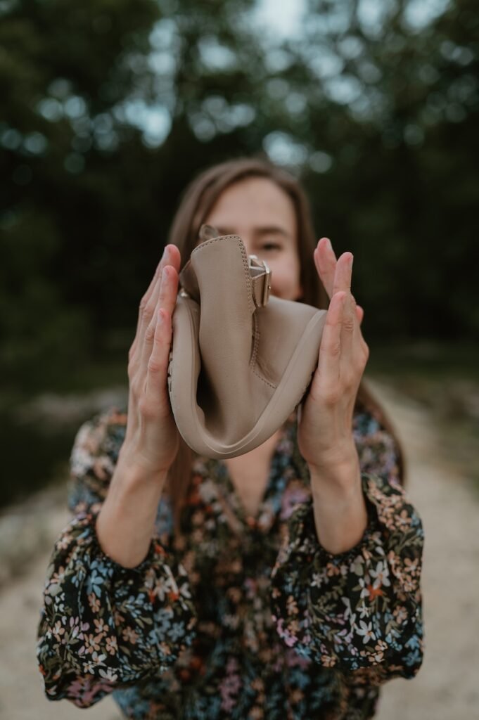 A woman squishing a Tari II barefoot buckle chelsea boot from Xero Shoes into a U shape to demonstrate the flexibility of the zero drop outsole. A floral blouse is blurred in the background.