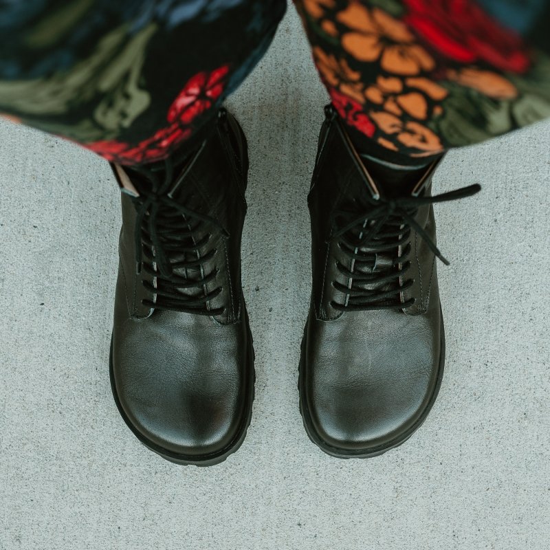 A top down look at a pair of Lang S Kombat leather lace up wide toe box boots. There is a floral utility suit visible at the top of the frame