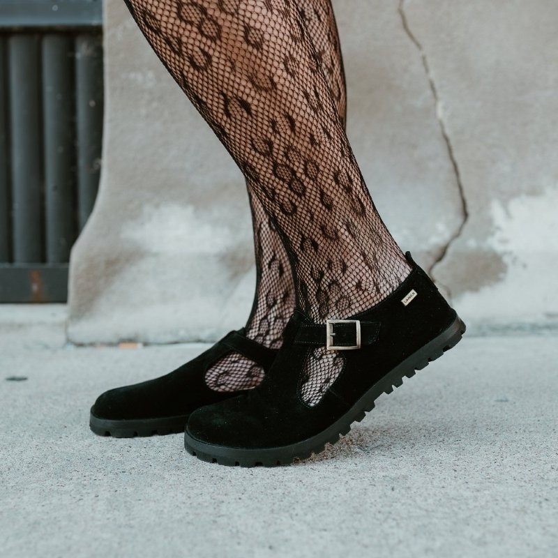 Side view of a woman's legs in Lang S barefoot T Strap flats with a wide toe box. Her legs are covered in lacey mesh tights and her front foot is flexed up slightly showing off the zero drop outsole