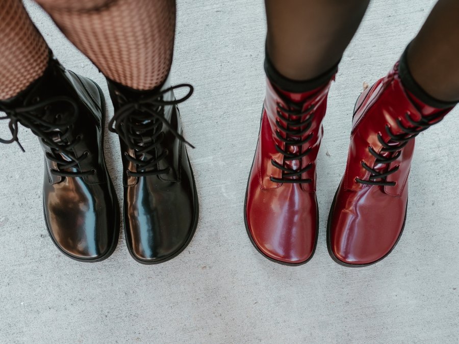 Top down view of two women's legs in Shapen Maverick, a wide toe box lace up combat style boot. The right pair is a bordeaux patent leather, and the black is a black patent leather