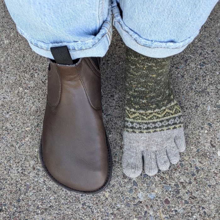 A top down view of a person with 1 Softstar Primal Chelsea boot on one foot, and the other foot with just a pair of toe socks to show the shape match. The extra wide toe box chelsea boot in brown leather is handmade in the USA.