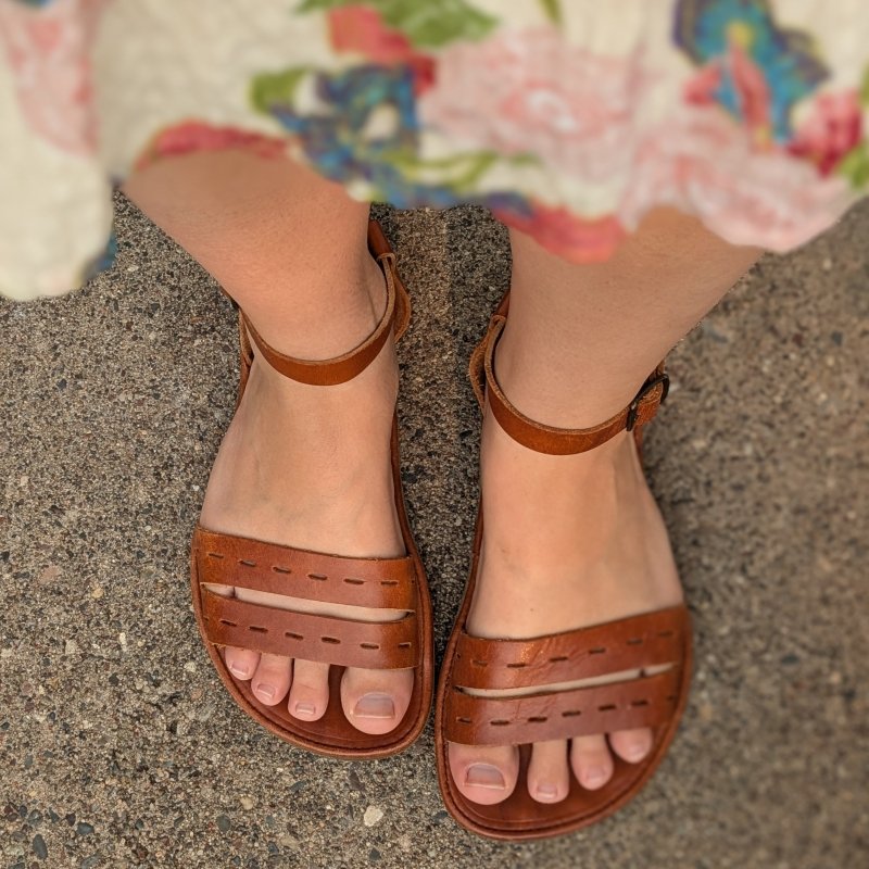 Close up top down view of a pair of Cut Here sandal from The Drifter Leather in a custom shape for hard to fit feet. A floral dress is visible at the top of the frame