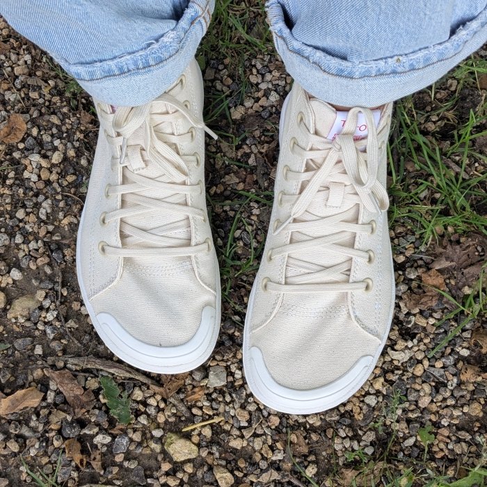 A pair of canvas high tops with an extra wide toe box seen from the top down, with cuffed light colored jeans hovering above the ankle. Tolos transition barefoot sneakers