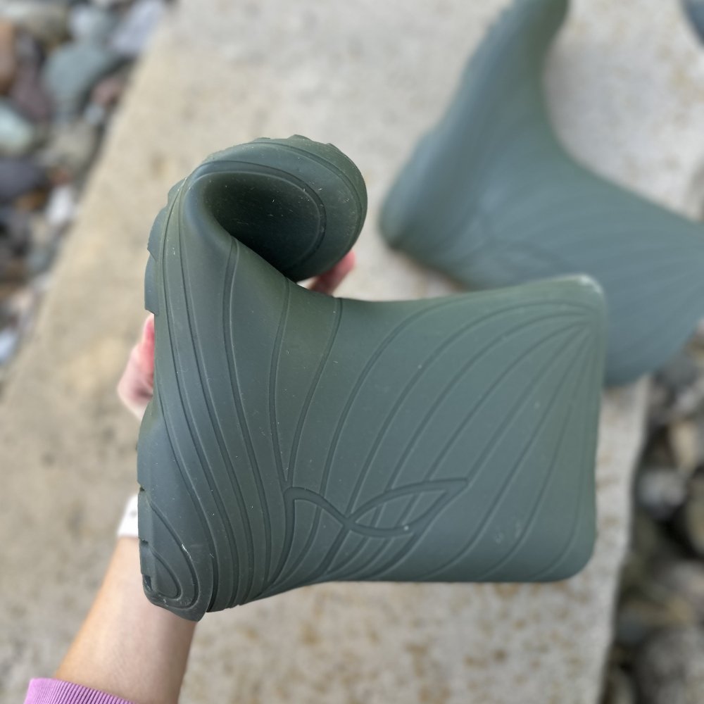 A hand flexing the toe up on a pair of Wildling Ranidae rubber barefoot rain boots to show the flexibility of the thin, zero drop outsole