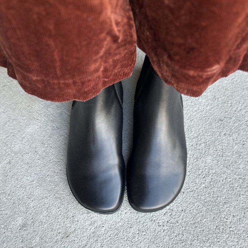 Top down view of a person in wide leg burnt orange corduroy pants wearing Zaqq Equity barefoot chelsea boots in black leather with a smooth top and wide toe box