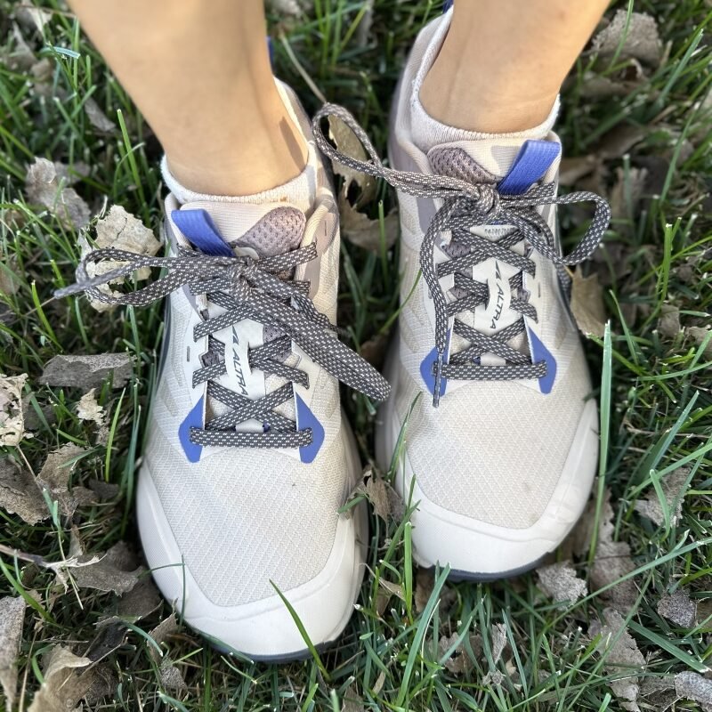 Top down close up of a pair of feet wearing Altra Lone Peak wide toe box sneaker in a white textile with purple accents