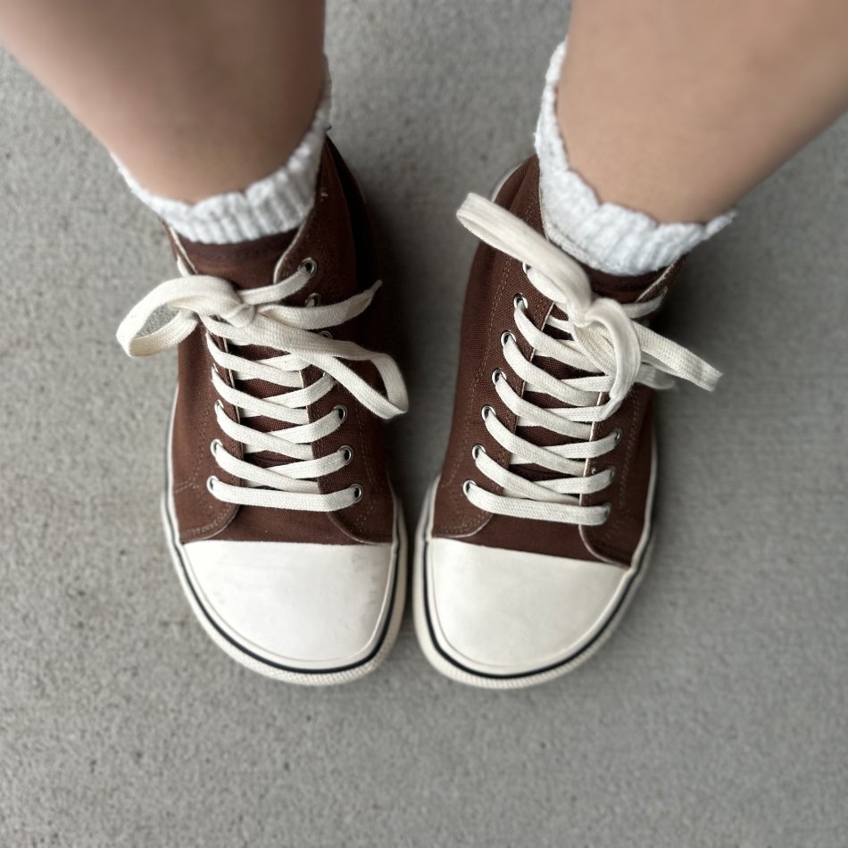 A pair of extra wide cap toe high tops in chocolate brown hemp canvas with off-white laces and accents, being worn with ruffled socks poking out the top