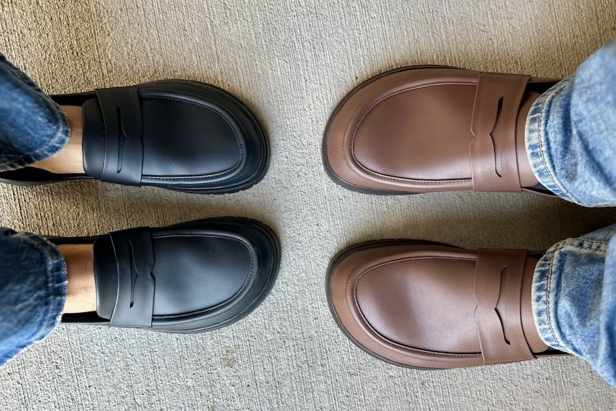 Two people in Feelgrounds Barefoot Loafers in vegan material standing toe to toe. The woman on the left is wearing them in black, and the man on the right is wearing brown.