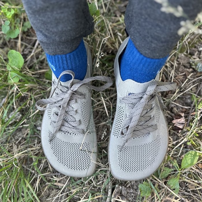 A close up pictures of a pair of Freet Keld 2 barefoot hiking shoes being worn on a hike with blue socks. The extra wide toe box in a knit material is in the forefront of the image.