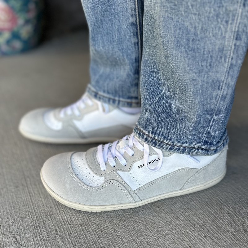 A side view of Groundies Nova sneakers in gray suede with white leather details. The barefoot plus model has an extra wide toe box and a GO1 thin flexible outsole.