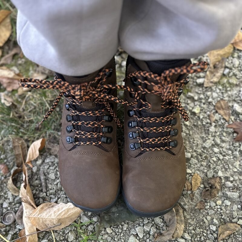 A close up of a pair of Groundies Portland hiking boots with a wide toe box, black and orange laces, and leather uppers.